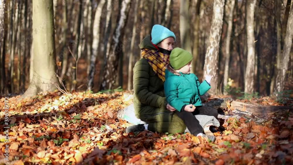 Little happy boy with young mother sitting near the fire enjoying autumn forest nature. Sunny background. Family healthcare. Green tourism. Traveling lifestyle. Weekend outdoor. Smiling male child. Little happy boy with young mother sitting near the fire enjoying autumn forest nature. Sunny background. Family healthcare. Green tourism. Traveling lifestyle. Weekend outdoor. Smiling male child.
