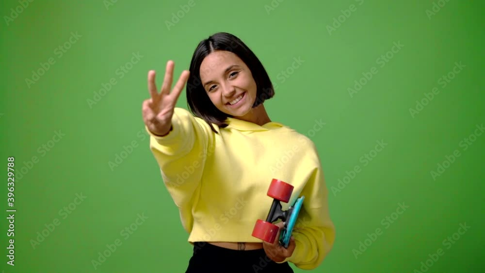Young skater woman on green screen chroma key background happy and counting with fingers Young skater woman on green screen chroma key background happy and counting with fingers