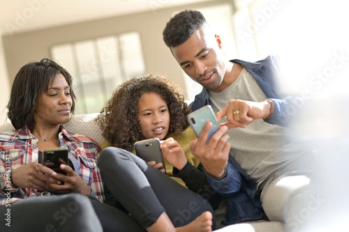 African-american family of three having fun playing with smartphones