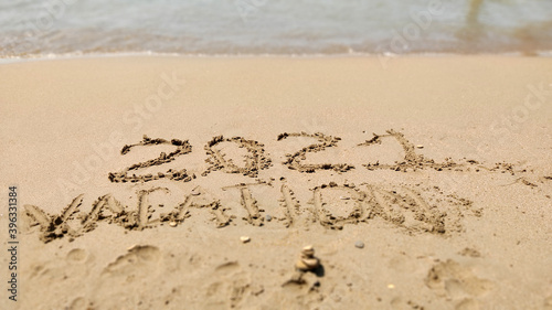 2021 Vacation handwritten inscription in sand of sea beach