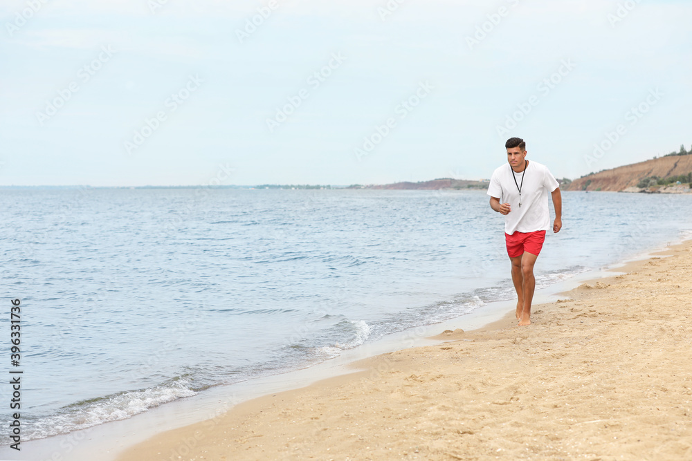 Handsome male lifeguard running on sandy beach