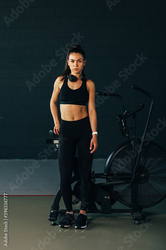 Portrait of a sportswoman looking at camera standing in gym at air bike