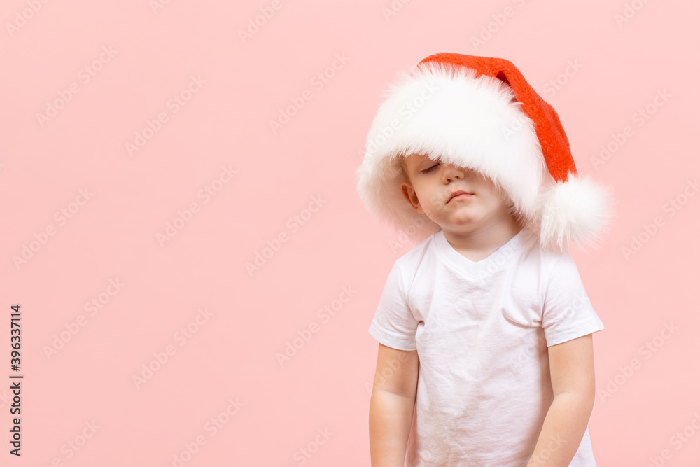 Sleeping Christmas tired child Santa Claus in hat with closed eyes on pink background. Studio shot concept about new year, vacation, holiday, preparation and celebration.