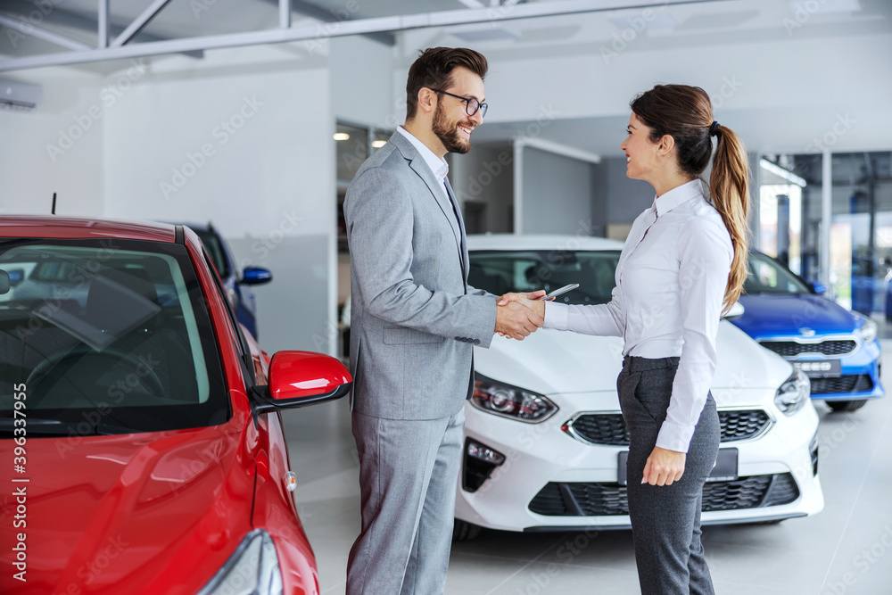 Excited car buyer with face mask shaking hands with car seller and taking car keys while sitting in car salon. Excited car buyer with face mask shaking hands with car seller and taking car keys while sitting in car salon.