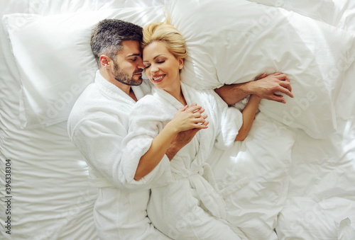 Top view of a middle-aged couple in love in bathrobes on honeymoon lying in a bed and cuddling.