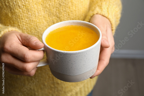 Woman holding cup with sea buckthorn tea on blurred background, closeup