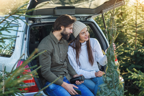 фотографія Pleasant couple sitting in car trunk and looking at wonderful christmas tree they choose for holidays at plantings area