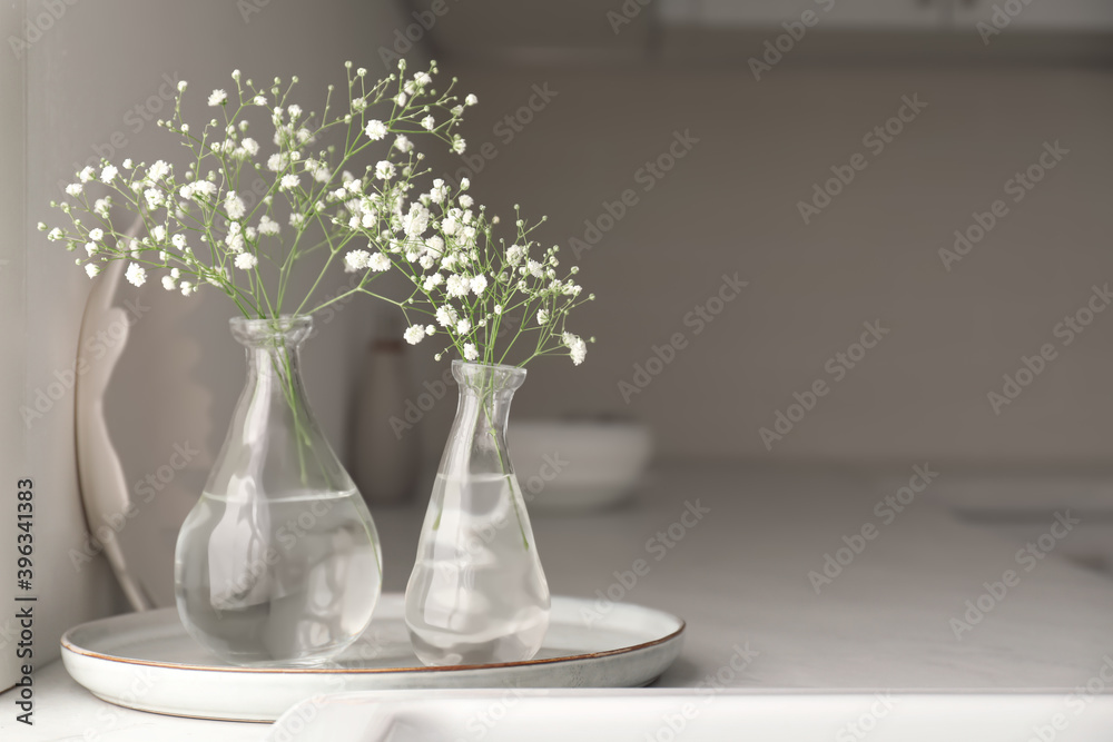 Vases with gypsophila flowers on countertop in kitchen, space for text. Interior design