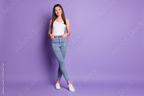 Full side photo of happy fit woman hold hands in pockets wear white singlet isolated on violet color background