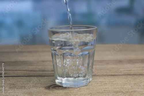 Fresh water pouring into glass on wooden table.Blurred background.
