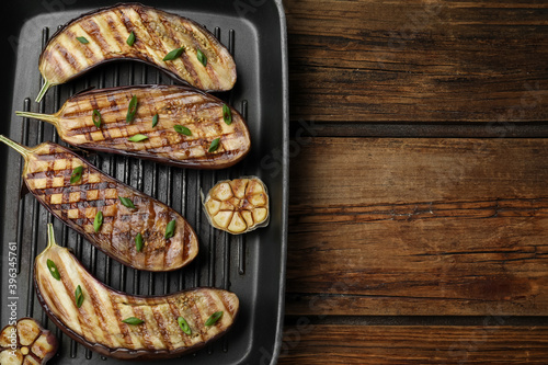 Delicious grilled eggplant halves in pan on wooden table, top view. Space for text