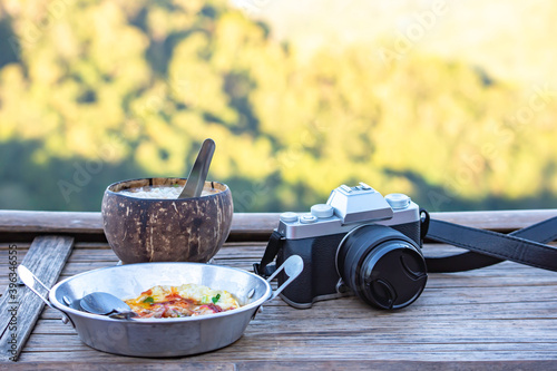 Fried eggs in a pan , Boiled rice in coconut shell and camera on a wooden table Background blurry views tree.