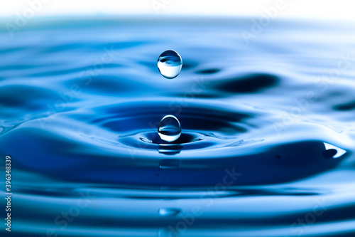 Dark blue water droplets splash in the water surface close up. Creating a perfect water wave