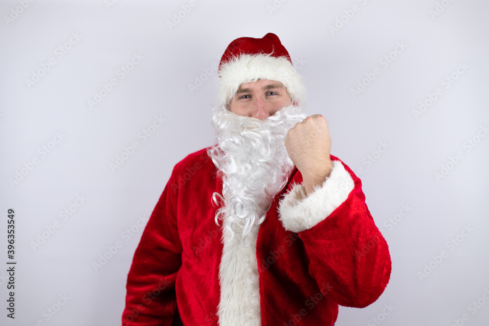Man dressed as Santa Claus standing over isolated white background angry and mad raising fist frustrated and furious while shouting with anger. Rage and aggressive concept. Man dressed as Santa Claus standing over isolated white background angry and mad raising fist frustrated and furious while shouting with anger. Rage and aggressive concept.