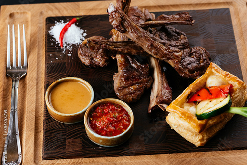 Canvas Print grilled lamb rack with vegetables and sauce on a black backgroun