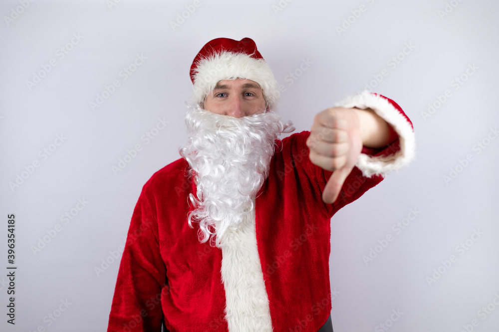Man dressed as Santa Claus standing over isolated white background with angry face, negative sign showing dislike with thumb down