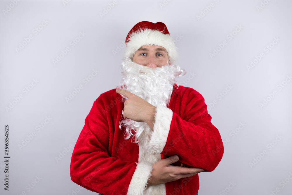 Man dressed as Santa Claus standing over isolated white background smiling confident pointing with hand and finger to the side Man dressed as Santa Claus standing over isolated white background smiling confident pointing with hand and finger to the side