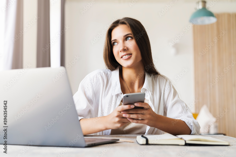 Attractive business woman sits at table in front of laptop and talks on mobile phone, negotiates on the phone. Attractive business woman sits at table in front of laptop and talks on mobile phone, negotiates on the phone.