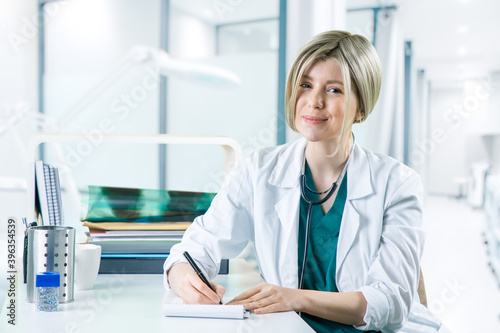 Female doctor sitting at desk at hospital writing prescription