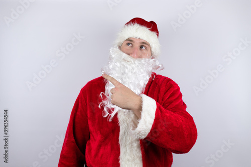 Man dressed as Santa Claus standing over isolated white background pointing with hand and finger to the side surprised