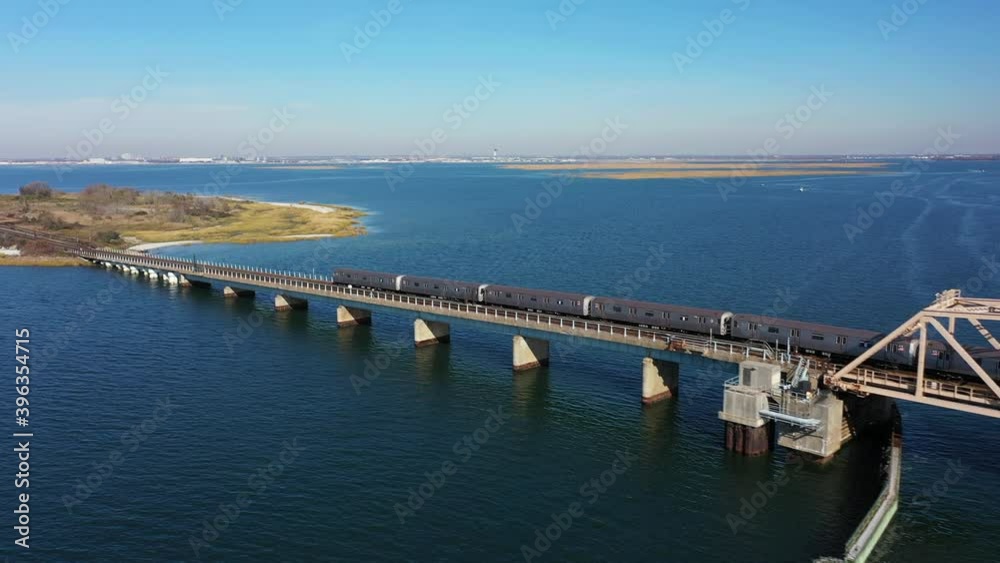 A high angle shot of a NYC subway train crossing over the bay in Queens, NY. The camera trucks left following the train. The sun is shining and it is a beautiful day. A high angle shot of a NYC subway train crossing over the bay in Queens, NY. The camera trucks left following the train. The sun is shining and it is a beautiful day.