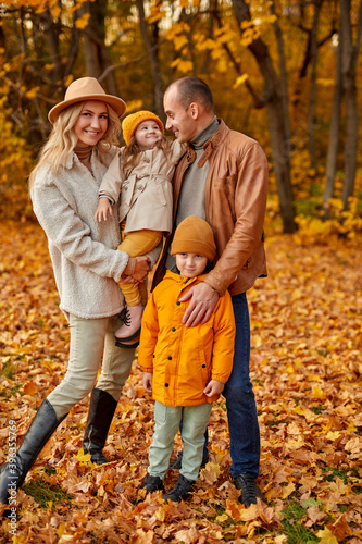 full-length portrait of lovely family with children in autumn sunny forest, caucasian parents and kids in coats posing at camera © alfa27