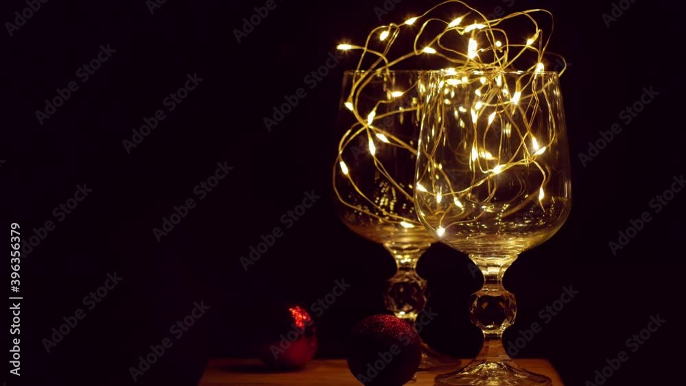 Crystal wine glasses decorated with golden glowing garland on Christmas table bokeh lights background. Romantic New Years eve dinner with champagne for couple in love. Magic winter holidays atmosphere Crystal wine glasses decorated with golden glowing garland on Christmas table bokeh lights background. Romantic New Years eve dinner with champagne for couple in love. Magic winter holidays atmosphere