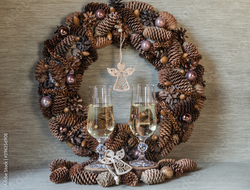 Glasses for wine with champagne, figurines of angels on the background of a Christmas wreath in a natural style. Christmas composition