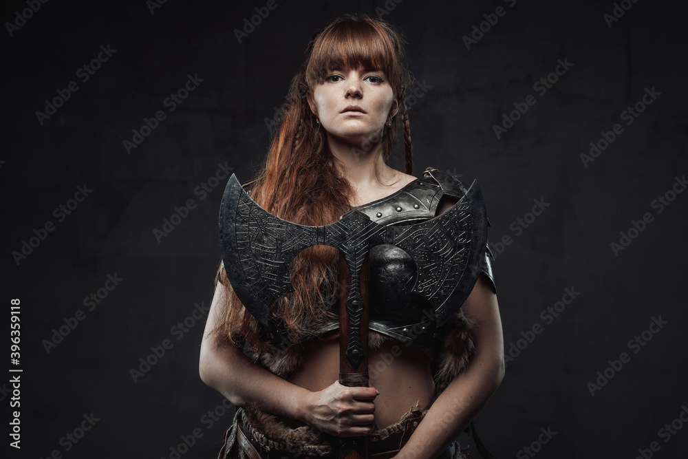 Beautiful but dangerous warlike woman viking with long brown hairs in dark armour holding huge axe in dark background. Beautiful but dangerous warlike woman viking with long brown hairs in dark armour holding huge axe in dark background.