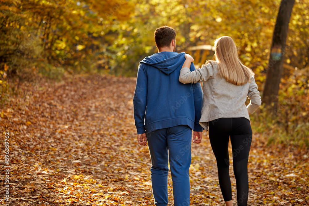 rear view on romantic young couple enjoying walk in the autumn sunny forest, contemplating the nature, yellow trees around. hiking, autumn forest, walking, love concept rear view on romantic young couple enjoying walk in the autumn sunny forest, contemplating the nature, yellow trees around. hiking, autumn forest, walking, love concept