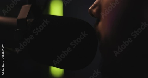 Close up of anonymous man in dimly lit studio environment speaking into microphone on boom arm. Slow motion (120 frames per second).