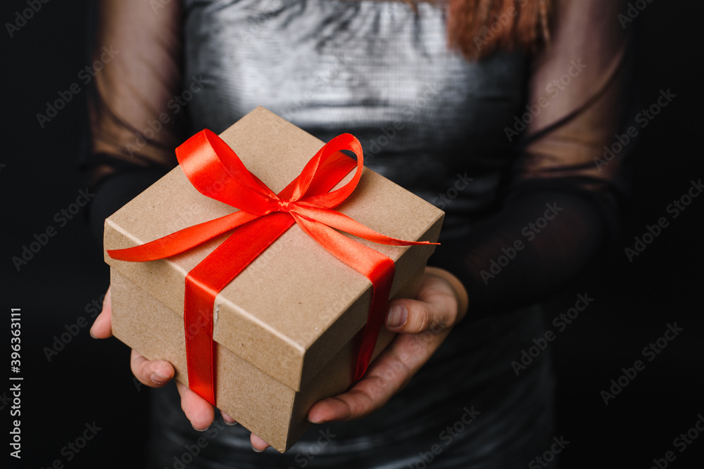 A young woman is holding a Christmas present with a red ribbon in her hands. Gift concept for the new year. Copy space A young woman is holding a Christmas present with a red ribbon in her hands. Gift concept for the new year. Copy space