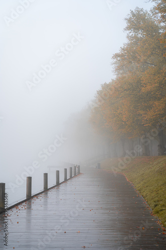 Foggy morning on the lake with wooden pier and walking person