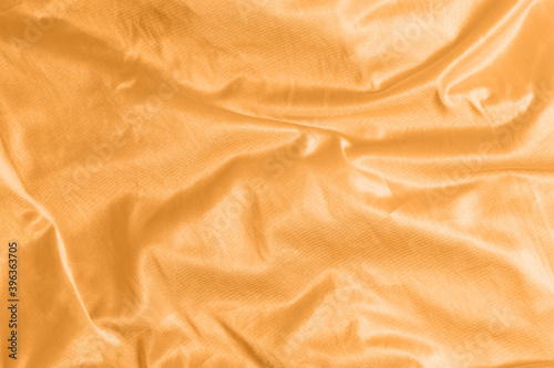 Shiny satin silk fabric with folds background texture textile. Tinted in 2021 color orange marigold.