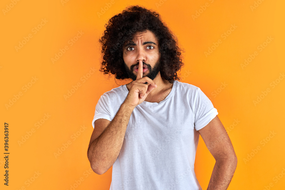 indian arabic male asking to be quiet with finger on lips, silence and secret concept. handsome guy keep silence, isolated over orange background indian arabic male asking to be quiet with finger on lips, silence and secret concept. handsome guy keep silence, isolated over orange background