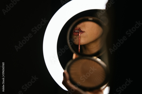 girl painting her lips through a lighted mirror