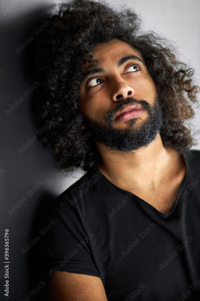 Fototapeta premium dreamy curly arabian male looking up, bearded guy is thinking about something , isolated black background