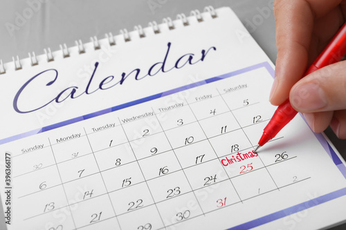 Woman writing word Christmas on calendar, closeup. Holiday countdown