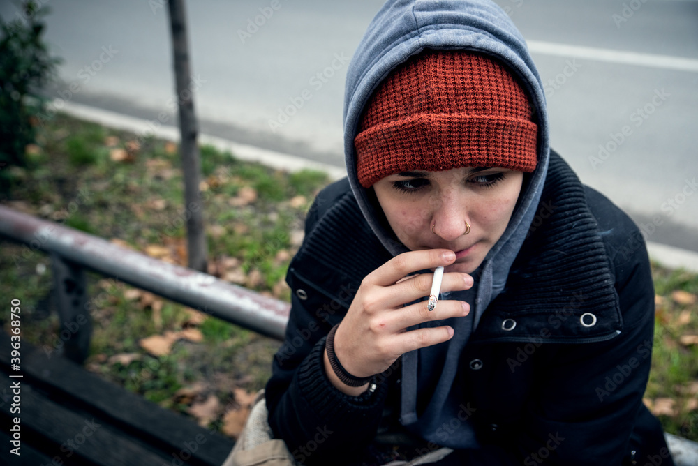 Very young homeless teenage girl sitting alone on the street in the cold weather and smoking the cigarette real people social documentary concept Very young homeless teenage girl sitting alone on the street in the cold weather and smoking the cigarette real people social documentary concept