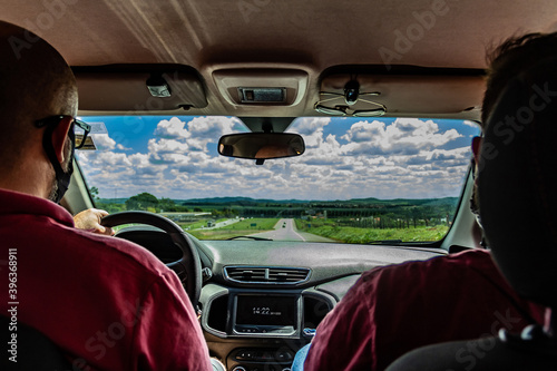 Dois homens dentro de um carro. Fotografia feita no interior do veículo.