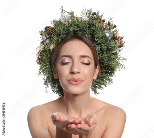 Beautiful young woman with Christmas wreath blowing kiss on white background