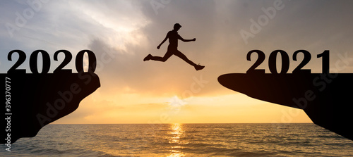 Abstract happy new year 2021 concept with silhouette man jumping from 2020 to 2021 at beautiful orange sky sunset over sea