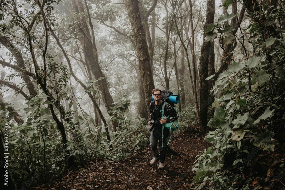 Young man hiking with backpack on in the foggy rainforest