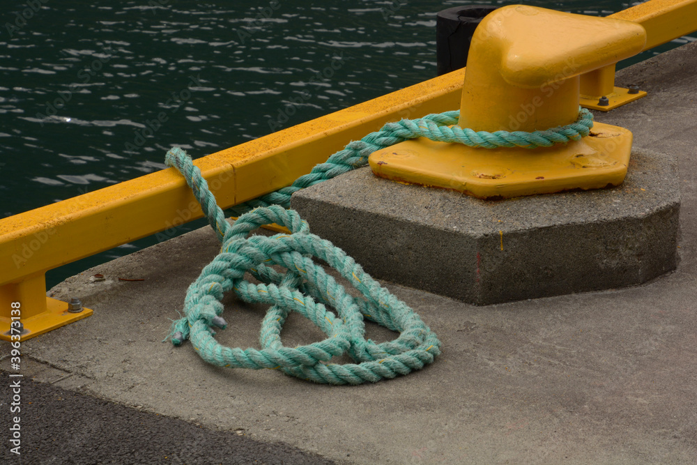 Fototapeta premium yellow bollard harbor on boat pier with green sea rope