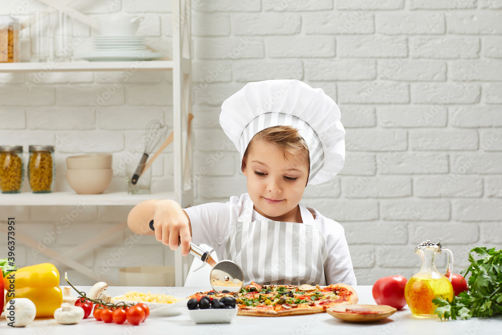 little boy in chef hat and an apron making homemade pizza in the kitchen. little boy in chef hat and an apron making homemade pizza in the kitchen.
