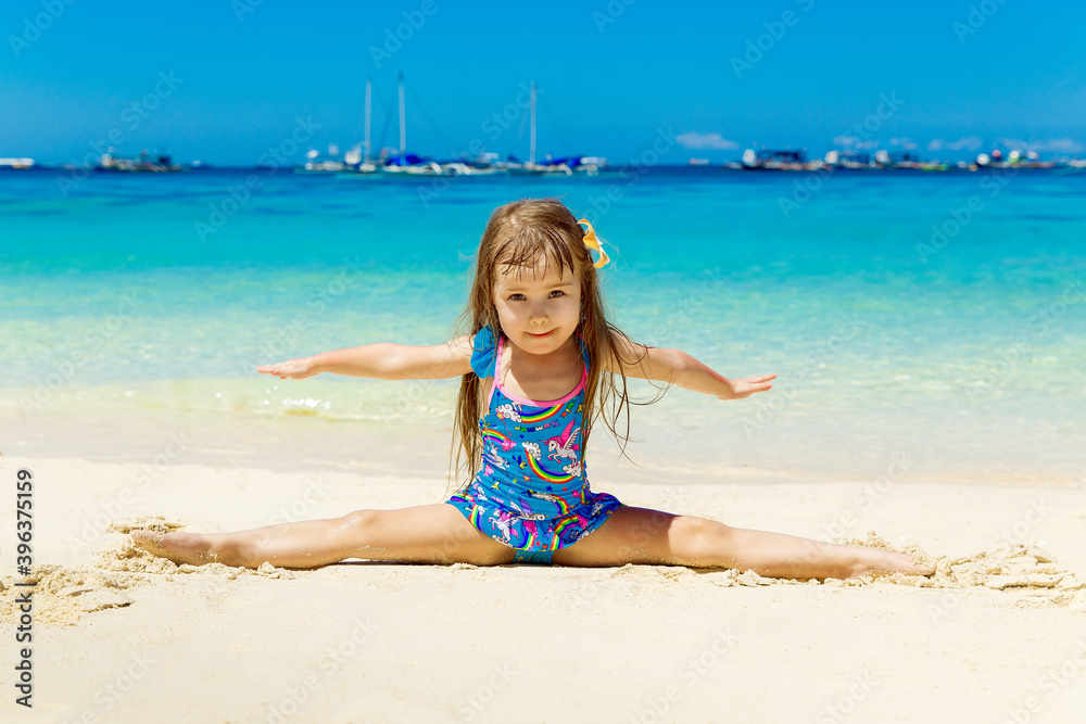 Smiling little girl doing gymnastics splits on a sandy tropical beach. The concept of travel and family holidays. Smiling little girl doing gymnastics splits on a sandy tropical beach. The concept of travel and family holidays.