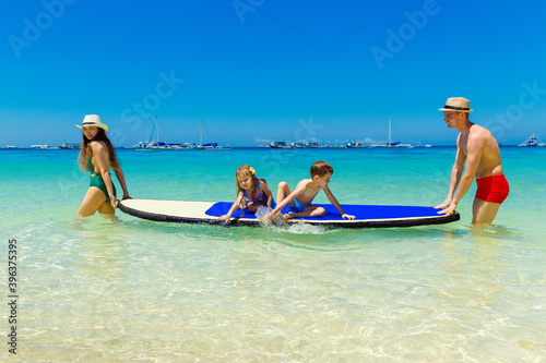 Happy family-mom, dad, little girl and boy have fun on a paddleboard in the tropical sea. The concept of travel and family holidays.