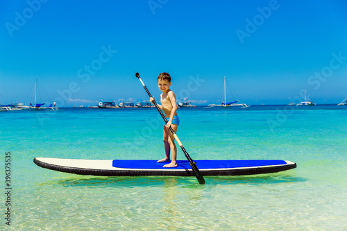 Happy little boy have fun on a paddleboard in the tropical sea. The concept of travel and family holidays.
