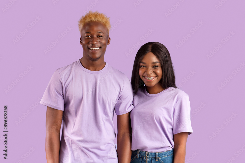 Obraz premium Positive African American couple smiling and looking at camera on violet studio background