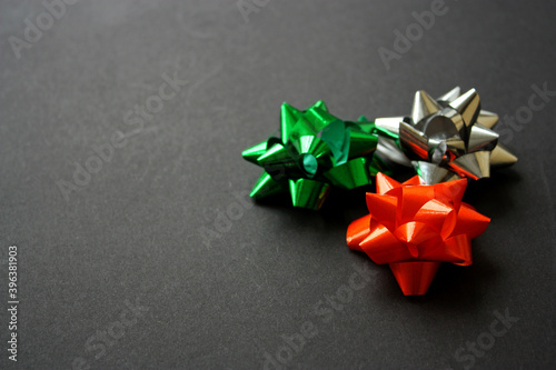 Festive shiny green, orange and silver gift bows for a present wrapping. Black background. Party decorations. New Year 2021. Christmas. Birthday. © Artemisia_Absinthium